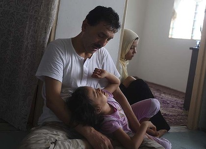 Hazara refugee Rajab plays with his eldest grandchild in the living room of their flat in Kuala Lumpur. Photo: Rahman Roslan